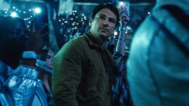 Josh Hartnett looks up as concertgoers hold their phones with flashlights lit.